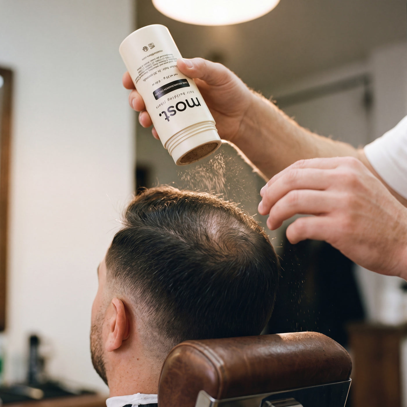 A barber applying most. hair building fibers to a client's thinning crown