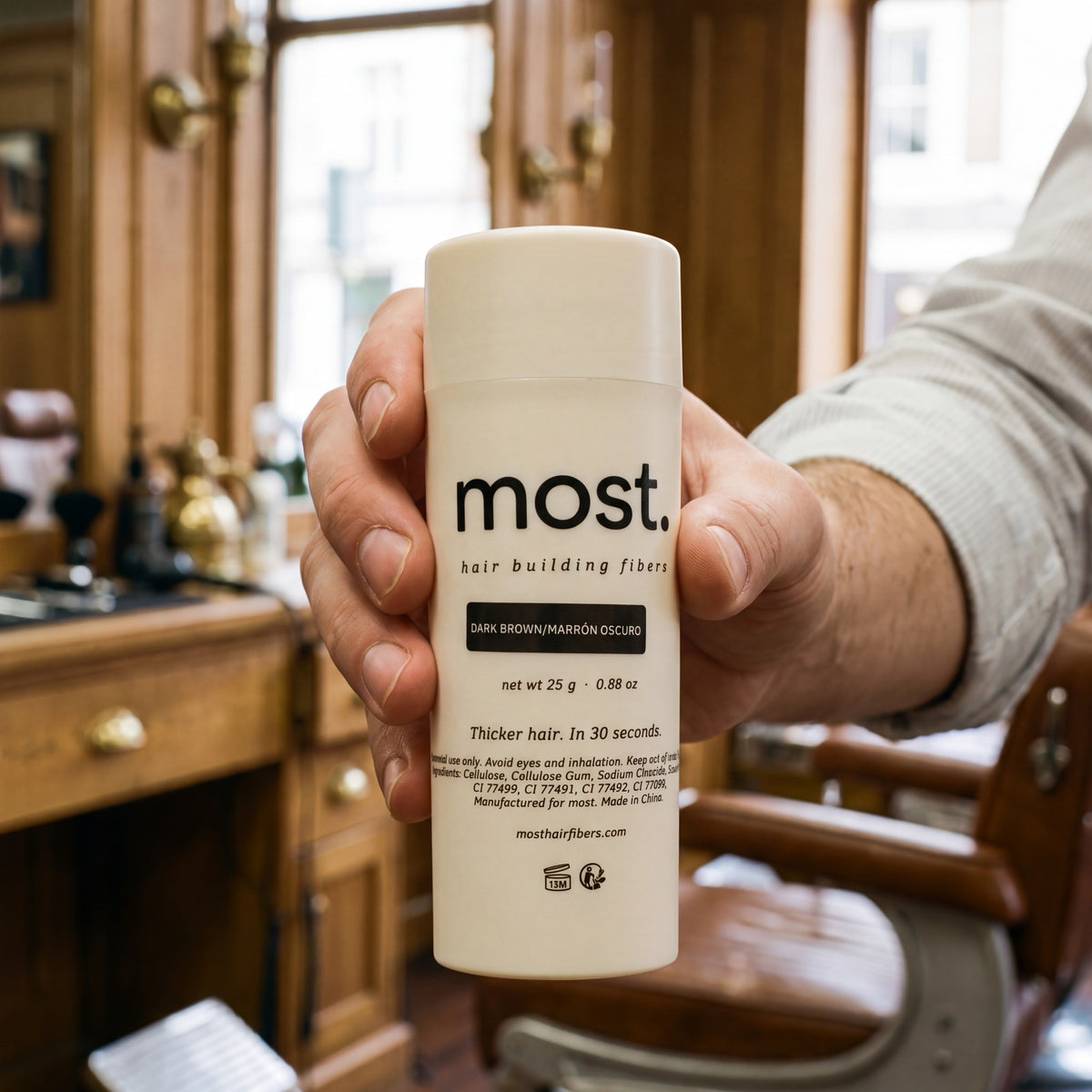 A hand holding a bottle of most. cotton hair building fibers in a barbershop