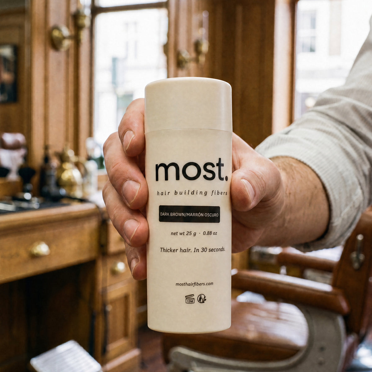 A hand holding a bottle of most. cotton hair building fibers in a barbershop